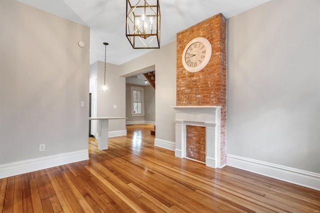 unfurnished living room featuring wood-type flooring, a chandelier, and a brick fireplace