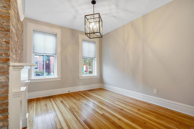 spare room with a large fireplace, light hardwood / wood-style flooring, a wealth of natural light, and an inviting chandelier