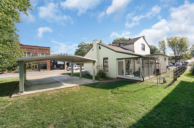 back of property with a carport, a sunroom, and a lawn