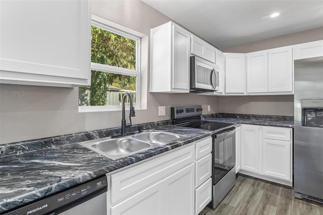 kitchen featuring appliances with stainless steel finishes, white cabinets, dark hardwood / wood-style flooring, dark stone counters, and sink