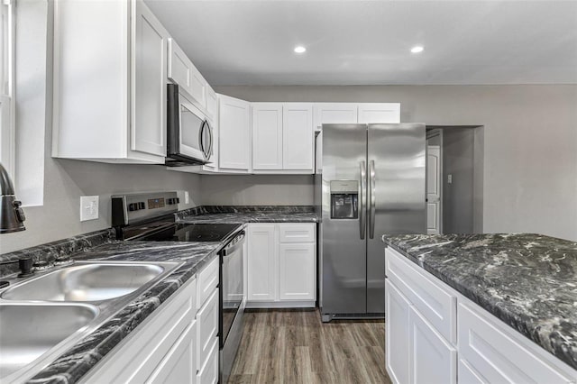 kitchen with white cabinets, sink, appliances with stainless steel finishes, dark hardwood / wood-style floors, and dark stone countertops