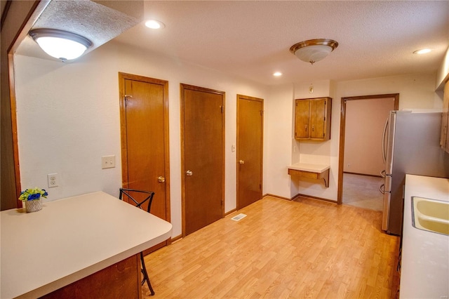 kitchen with light wood-type flooring, stainless steel refrigerator, a textured ceiling, and a breakfast bar area