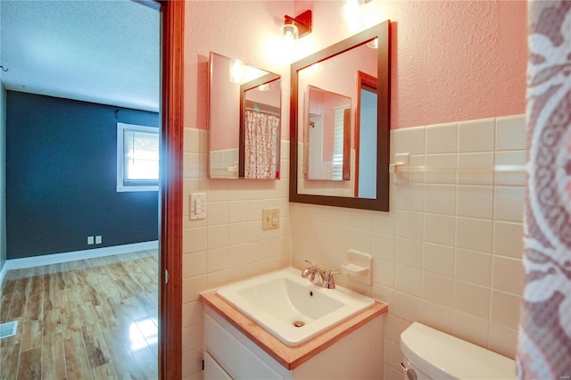 bathroom featuring vanity, a textured ceiling, hardwood / wood-style flooring, tile walls, and toilet