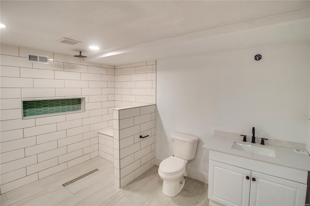 bathroom with tiled shower, vanity, and toilet