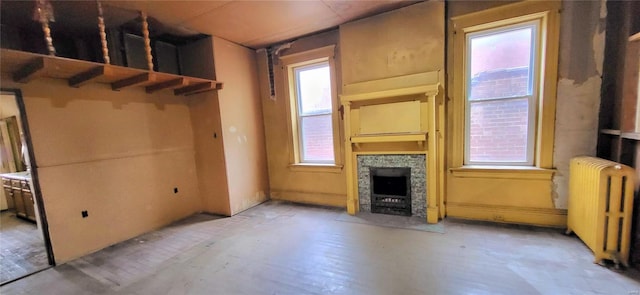 unfurnished living room with radiator heating unit, hardwood / wood-style flooring, a healthy amount of sunlight, and a stone fireplace