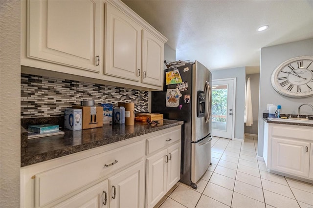 kitchen featuring tasteful backsplash, sink, white cabinetry, light tile patterned floors, and stainless steel fridge