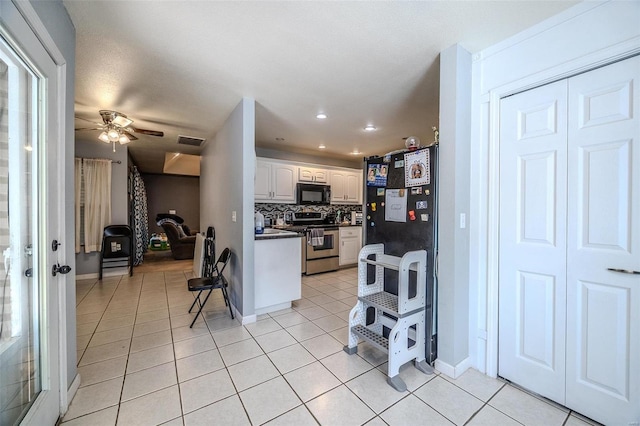 kitchen featuring ceiling fan, light tile patterned flooring, backsplash, white cabinetry, and stainless steel stove