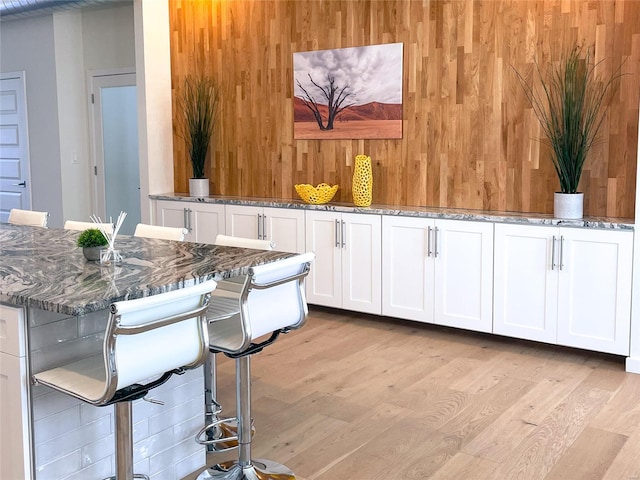 kitchen featuring light wood-type flooring, a breakfast bar, dark stone countertops, and white cabinets