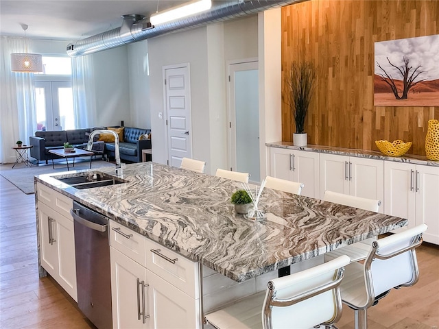 kitchen featuring light stone counters, light hardwood / wood-style floors, sink, white cabinets, and a kitchen breakfast bar