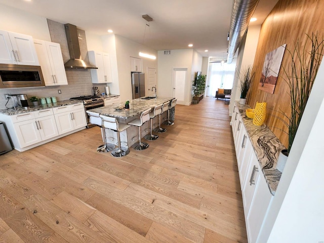 kitchen with light stone counters, white cabinets, wall chimney exhaust hood, stainless steel appliances, and light wood-type flooring