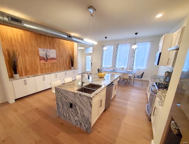 kitchen with light hardwood / wood-style floors, a kitchen island with sink, stainless steel appliances, and decorative light fixtures