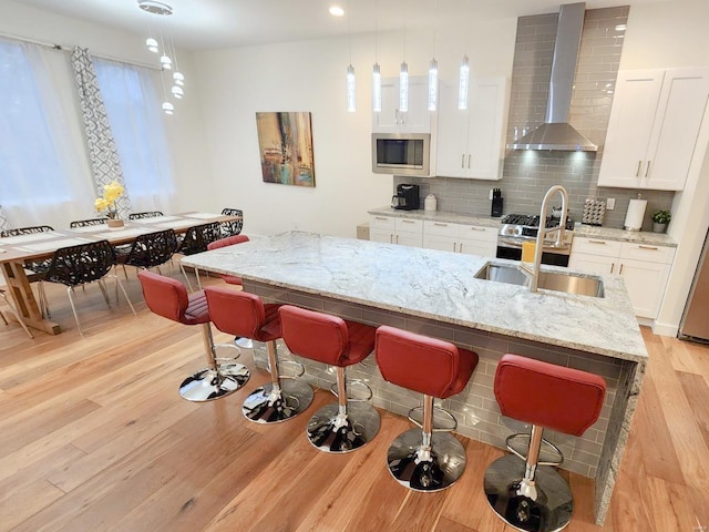 kitchen with pendant lighting, light stone counters, white cabinets, stainless steel microwave, and wall chimney exhaust hood