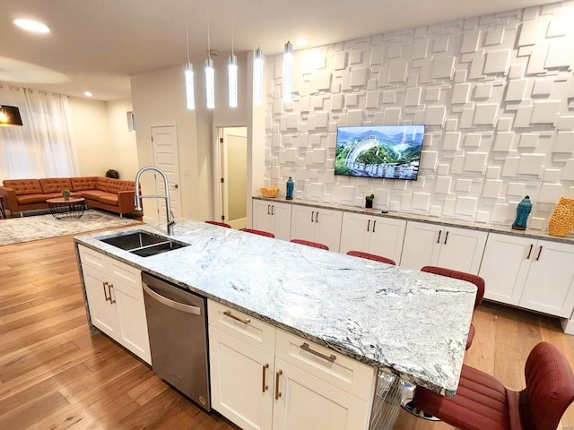 kitchen featuring stainless steel dishwasher, sink, light hardwood / wood-style flooring, and decorative light fixtures