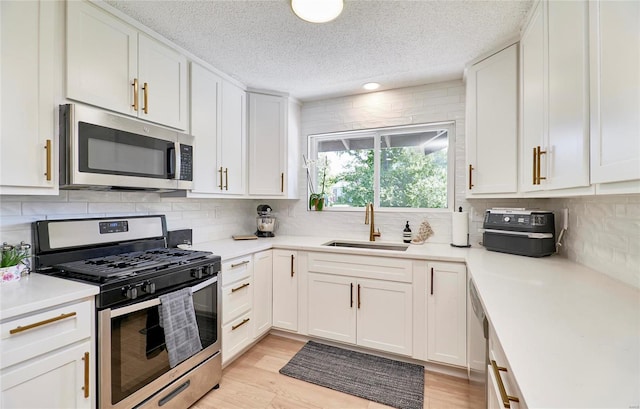 kitchen with light wood-type flooring, stainless steel appliances, white cabinetry, and sink