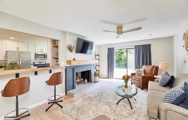 living room featuring ceiling fan, a fireplace, light hardwood / wood-style floors, and a textured ceiling