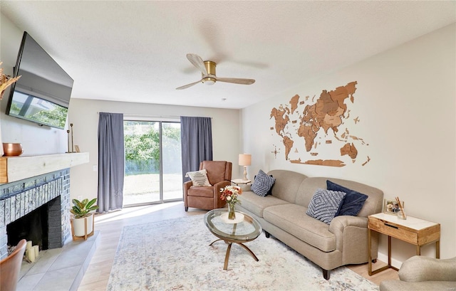 living room with a textured ceiling, ceiling fan, light hardwood / wood-style floors, and a fireplace