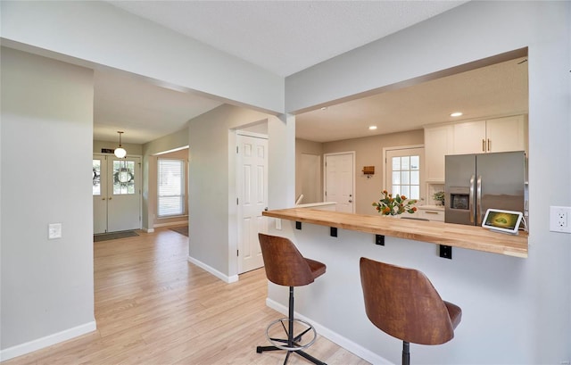 kitchen with a breakfast bar, wooden counters, hanging light fixtures, stainless steel fridge with ice dispenser, and white cabinetry