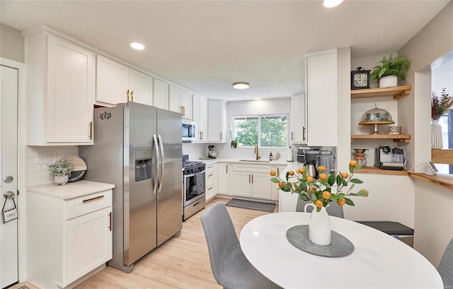 kitchen with white cabinetry, sink, backsplash, appliances with stainless steel finishes, and light wood-type flooring