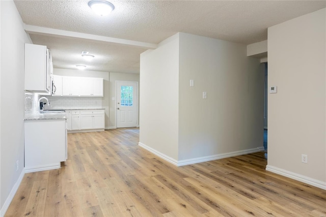 kitchen featuring white cabinets, a textured ceiling, light wood-type flooring, and backsplash