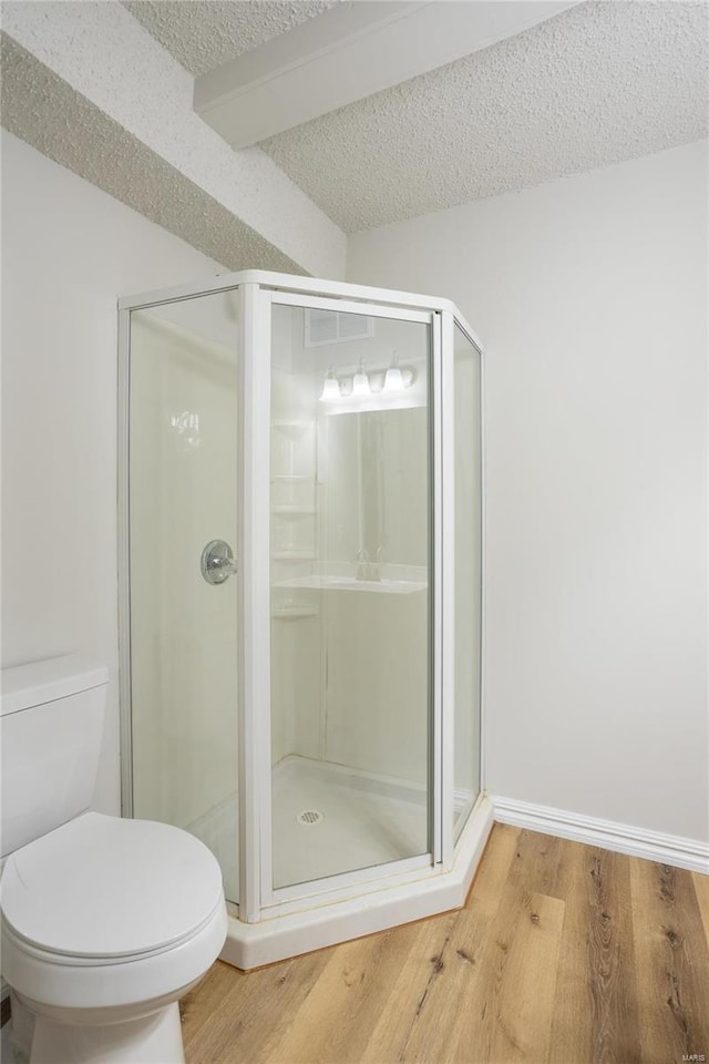 bathroom featuring a textured ceiling, wood-type flooring, toilet, and a shower with shower door