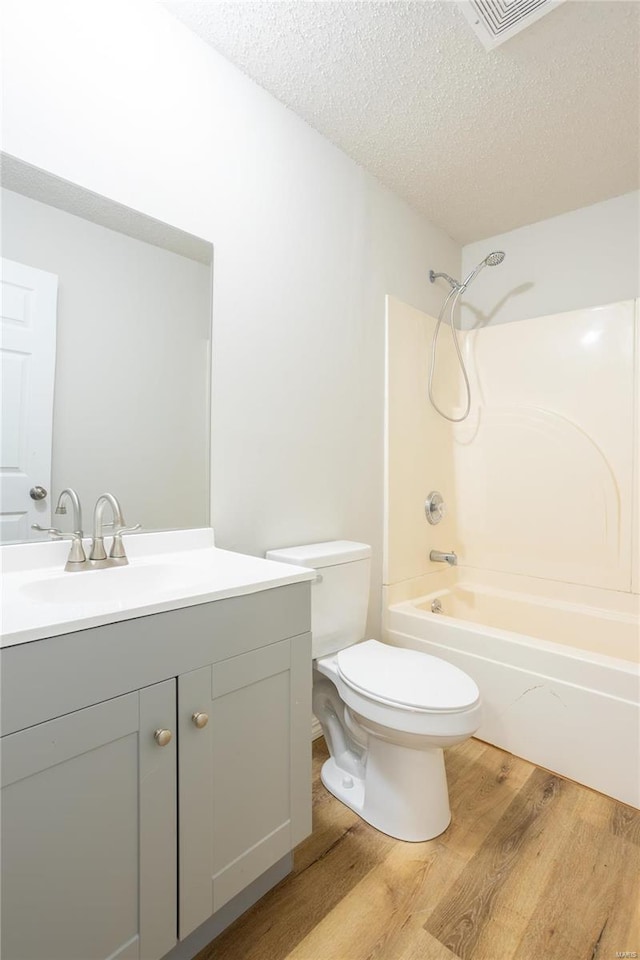 full bathroom featuring a textured ceiling,  shower combination, hardwood / wood-style floors, vanity, and toilet