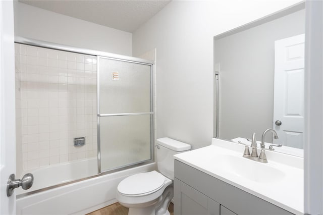 full bathroom with a textured ceiling, bath / shower combo with glass door, vanity, and toilet