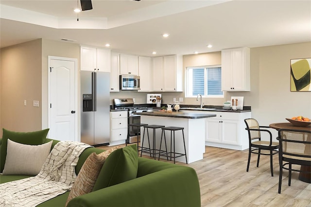 kitchen with sink, appliances with stainless steel finishes, white cabinetry, light hardwood / wood-style floors, and a kitchen bar