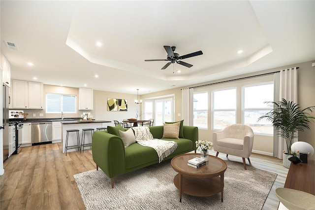 living room with ceiling fan, a tray ceiling, and light hardwood / wood-style flooring