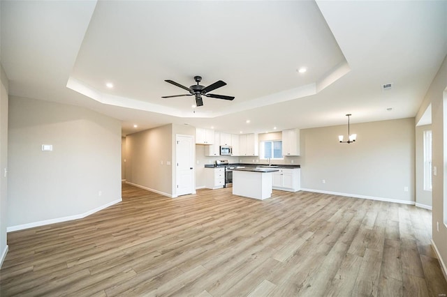 unfurnished living room featuring sink, ceiling fan with notable chandelier, a raised ceiling, and light wood-type flooring