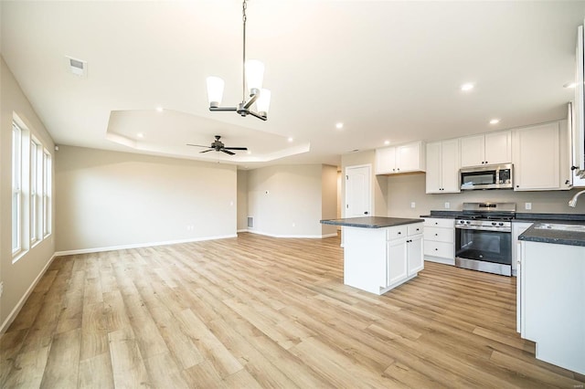 kitchen with a raised ceiling, appliances with stainless steel finishes, white cabinets, and decorative light fixtures