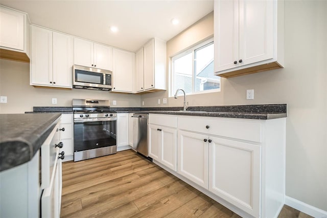 kitchen with appliances with stainless steel finishes, sink, light hardwood / wood-style flooring, and white cabinets