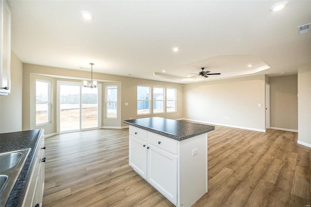 kitchen with decorative light fixtures, white cabinets, a center island, light hardwood / wood-style floors, and a healthy amount of sunlight