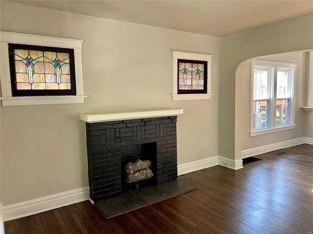 unfurnished living room with a brick fireplace and dark wood-type flooring