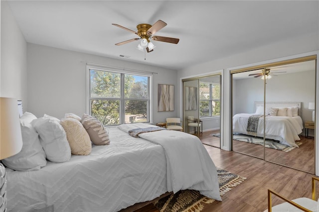 bedroom with ceiling fan, light hardwood / wood-style flooring, and two closets