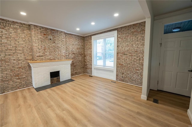 unfurnished living room with crown molding, light hardwood / wood-style floors, a brick fireplace, and brick wall