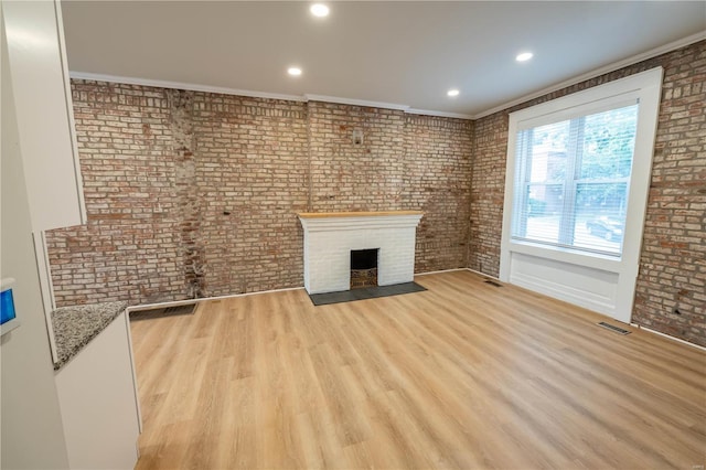 unfurnished living room with brick wall, crown molding, and light hardwood / wood-style floors