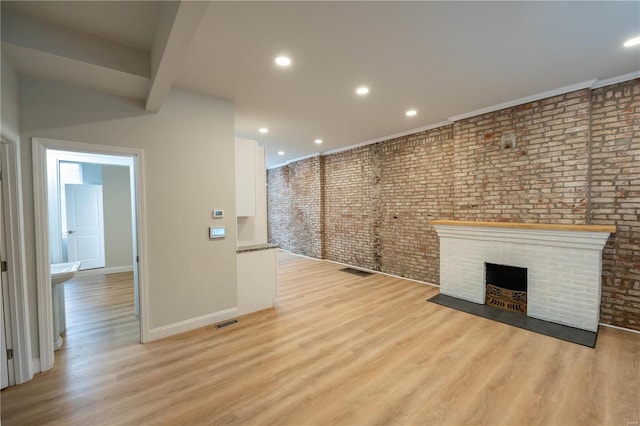 unfurnished living room with beamed ceiling, light hardwood / wood-style floors, and brick wall