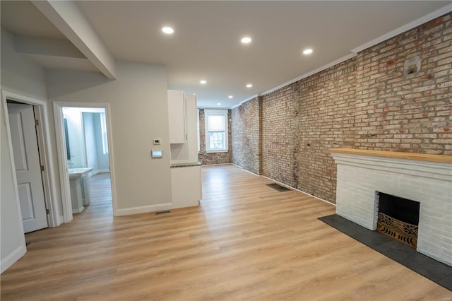 unfurnished living room with a fireplace, ornamental molding, light hardwood / wood-style flooring, and brick wall