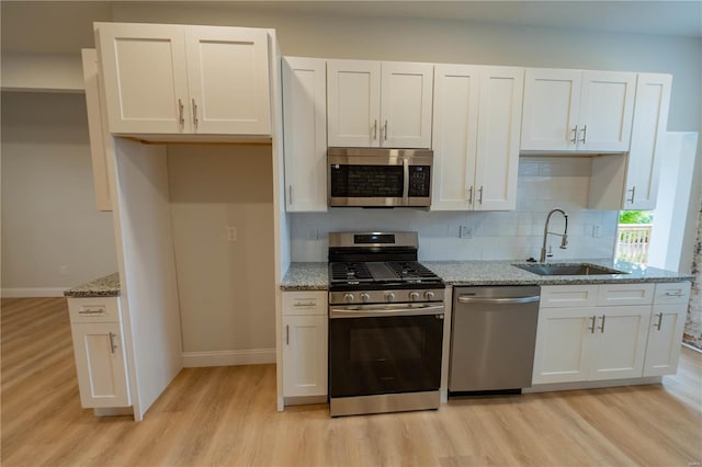 kitchen with light stone counters, light hardwood / wood-style floors, sink, white cabinetry, and appliances with stainless steel finishes