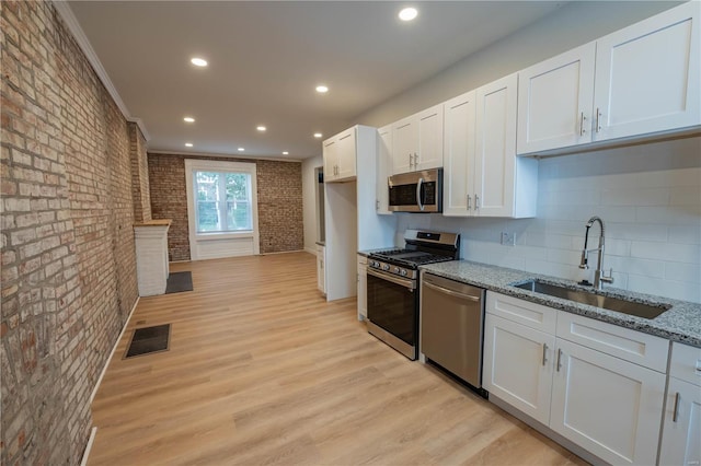 kitchen with white cabinetry, appliances with stainless steel finishes, light stone counters, and sink