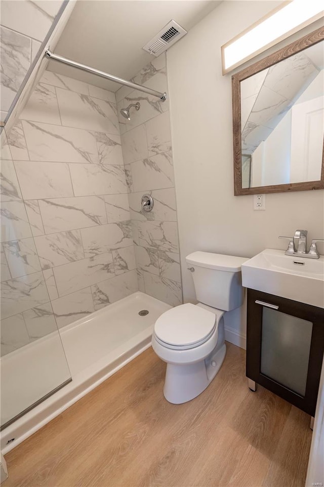 bathroom featuring a tile shower, hardwood / wood-style flooring, vanity, and toilet