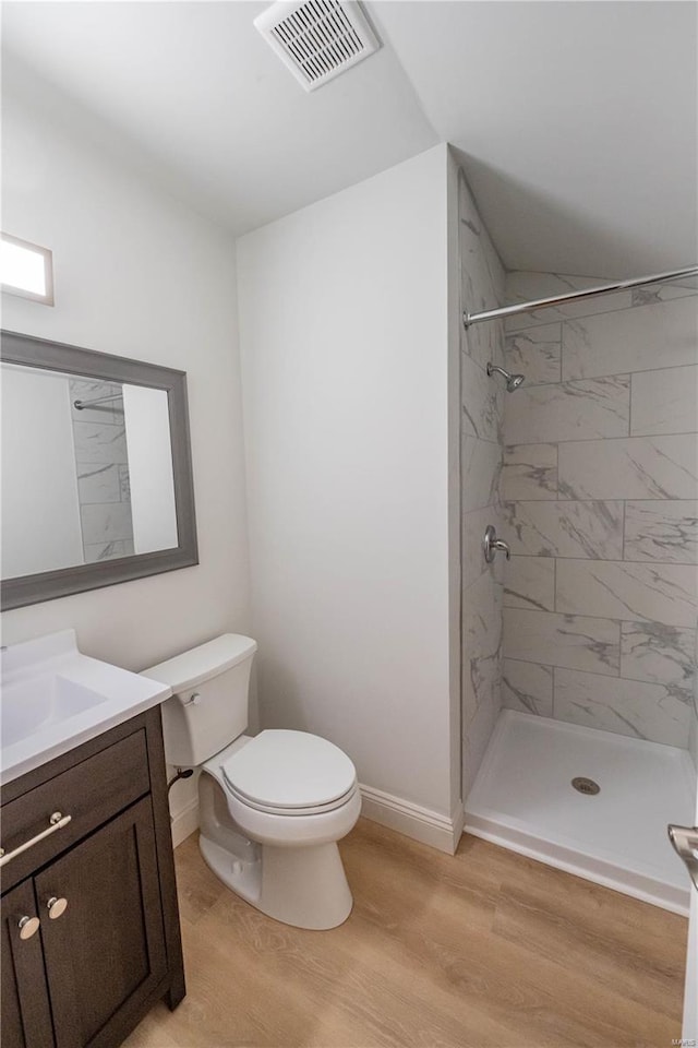 bathroom with a tile shower, vanity, toilet, and hardwood / wood-style flooring