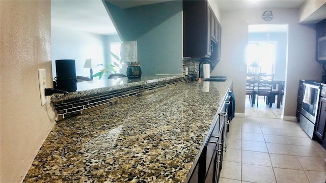 kitchen with light tile patterned flooring, stainless steel electric stove, dark stone countertops, sink, and decorative backsplash