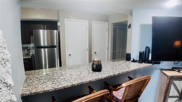 kitchen featuring stainless steel refrigerator, light stone countertops, kitchen peninsula, and a breakfast bar