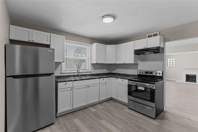 kitchen with appliances with stainless steel finishes, light hardwood / wood-style floors, white cabinetry, tasteful backsplash, and sink