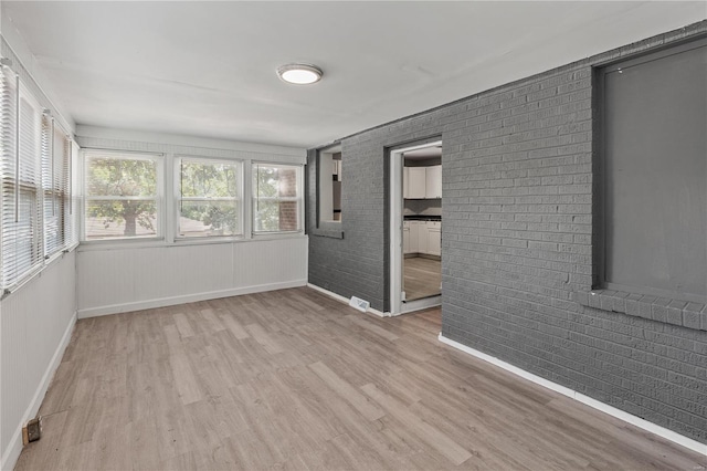 spare room with brick wall and light hardwood / wood-style flooring