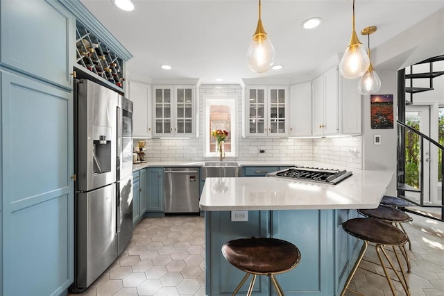 kitchen featuring appliances with stainless steel finishes, decorative light fixtures, white cabinets, blue cabinets, and a breakfast bar area