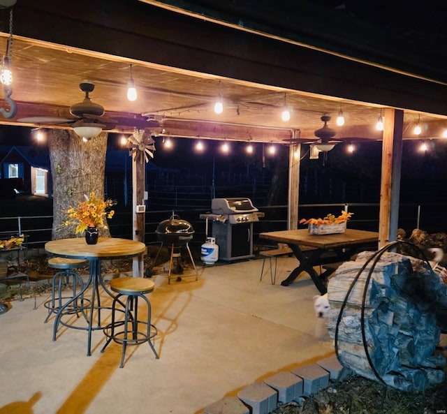 patio at night featuring grilling area, a ceiling fan, and outdoor dining area