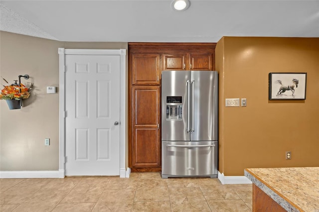 kitchen featuring light tile patterned floors, baseboards, light countertops, brown cabinetry, and high end refrigerator