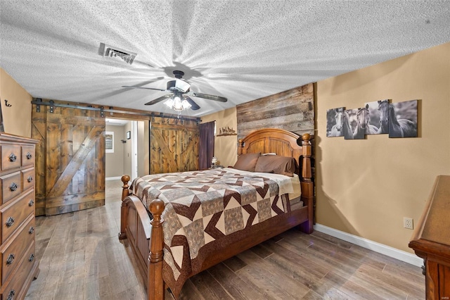 bedroom with baseboards, light wood finished floors, a barn door, and a textured ceiling